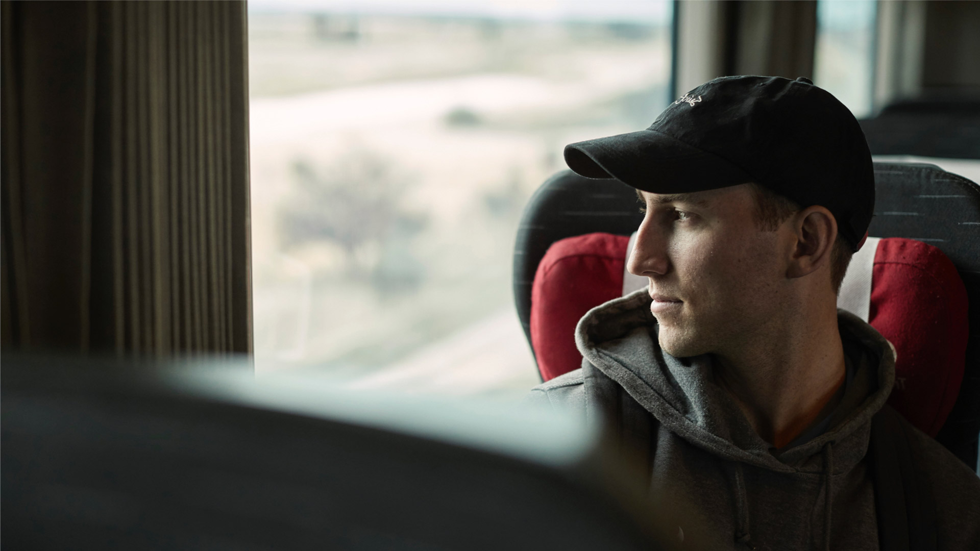 Man wearing baseball cap looking out train window